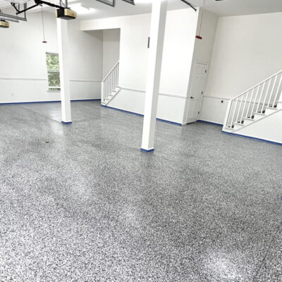 Spacious garage interior with a shiny speckled epoxy floor coating, white walls, and two staircases leading to upper levels. Large windows provide natural light. Spacious garage interior with a shiny speckled epoxy floor coating, white walls, and two staircases leading to upper levels. Large windows provide natural light.
