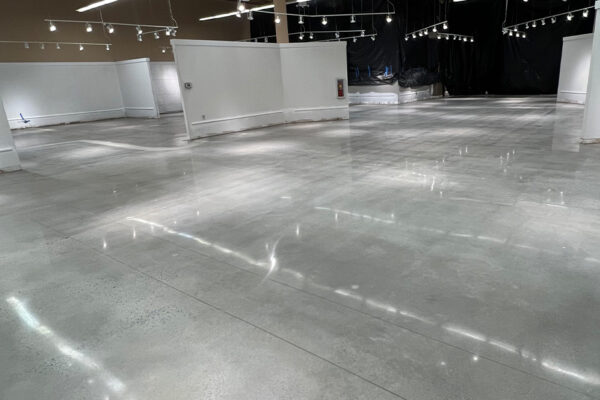 A large, empty room with polished epoxy floors and white walls, lit by numerous overhead lights with exposed black ceilings. A large, empty room with polished epoxy floors and white walls, lit by numerous overhead lights with exposed black ceilings.