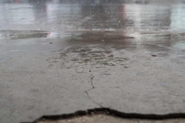 Close-up of a cracked concrete surface with visible water droplets reflecting light, indicating recent rainfall.