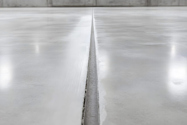 Close-up of a polished concrete floor with a narrow expansion joint running through the center. Reflections of overhead lights are visible on the surface.